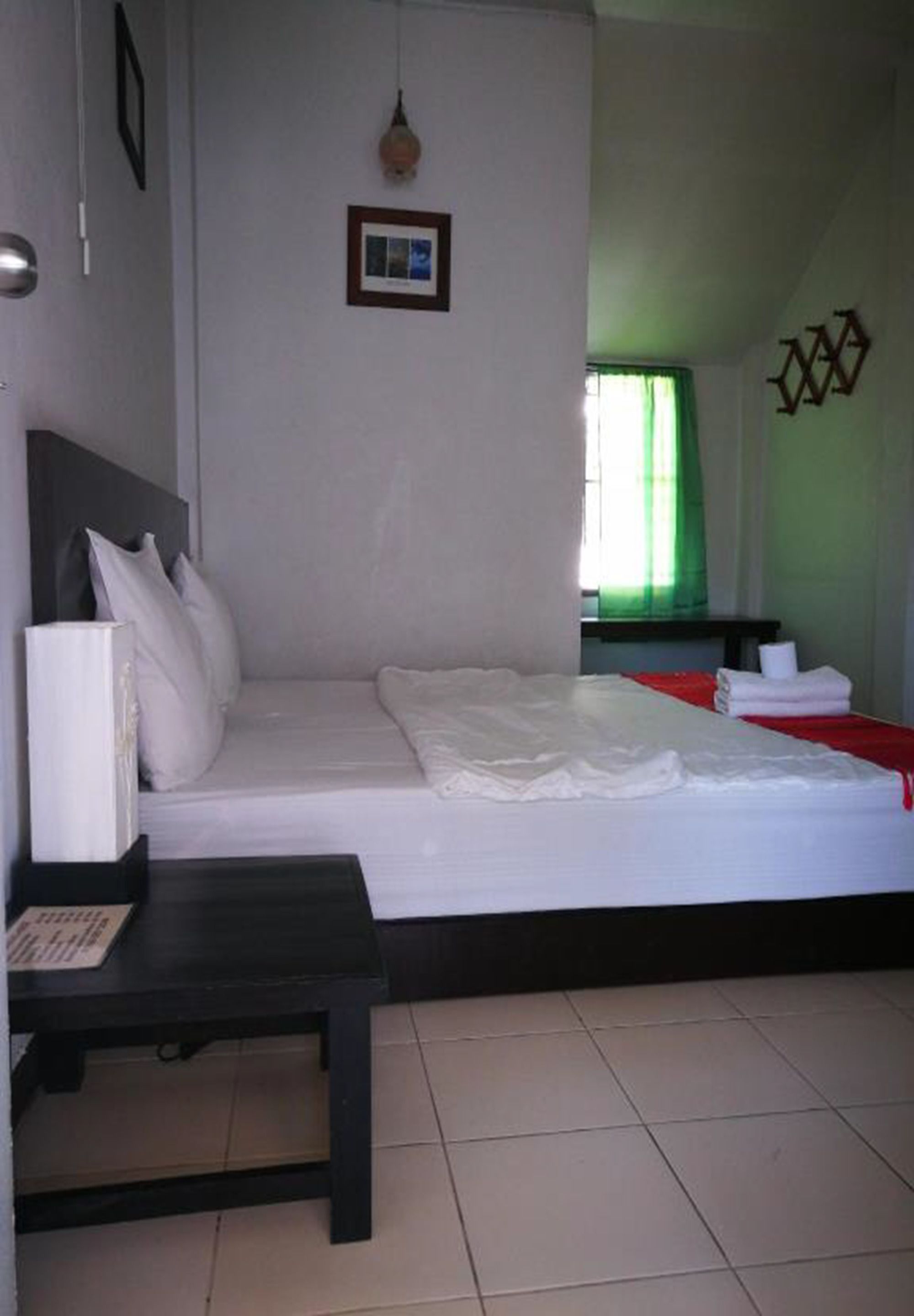 Quarto de hotel com cama, mesa de cabeceira, luminária na parede e janela com cortinas.