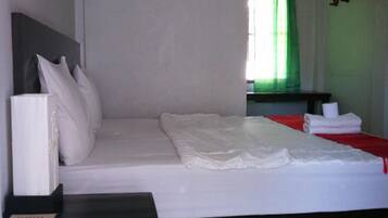 Une chambre d’hôtel avec un lit, une table de chevet, une lampe fixée au mur et une fenêtre avec des rideaux.