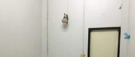 A small, single-bed room with a bed, a bedside table, a fan, and a door.