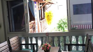 A covered outdoor seating area with wooden benches and tables, a decorative hanging lantern, and large windows providing a view of the outside. - Ampawan Guesthouse (Chiang Mai)