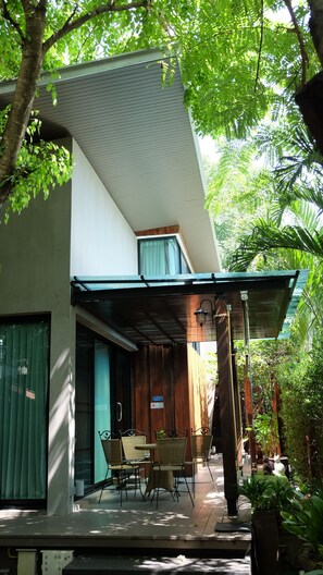 Una casa moderna con porche cubierto, mobiliario exterior y abundante vegetación.