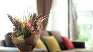 A living room with a sofa, a coffee table with a vase of flowers, and a window with curtains. - The White Elephant Home (Chiang Mai)