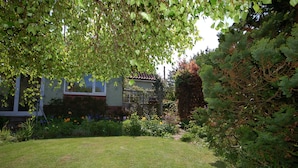 A garden with a lawn, a variety of plants, and a building with a tiled roof. - Walma has become a firm favourite with holidaymakers , a perfect retreat for family and friends. (Cromer)