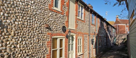 A narrow cobblestone street lined with traditional stone and brick buildings, featuring multiple windows and doors.