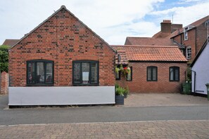 A brick building with a pitched roof and two windows with shutters.