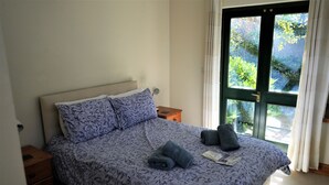 Una cama bien hecha con una colcha estampada con motivos florales, dos almohadas y toallas dobladas.