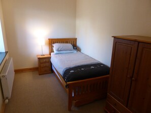 A bedroom with a wooden bed, a nightstand with a lamp, and a wardrobe.