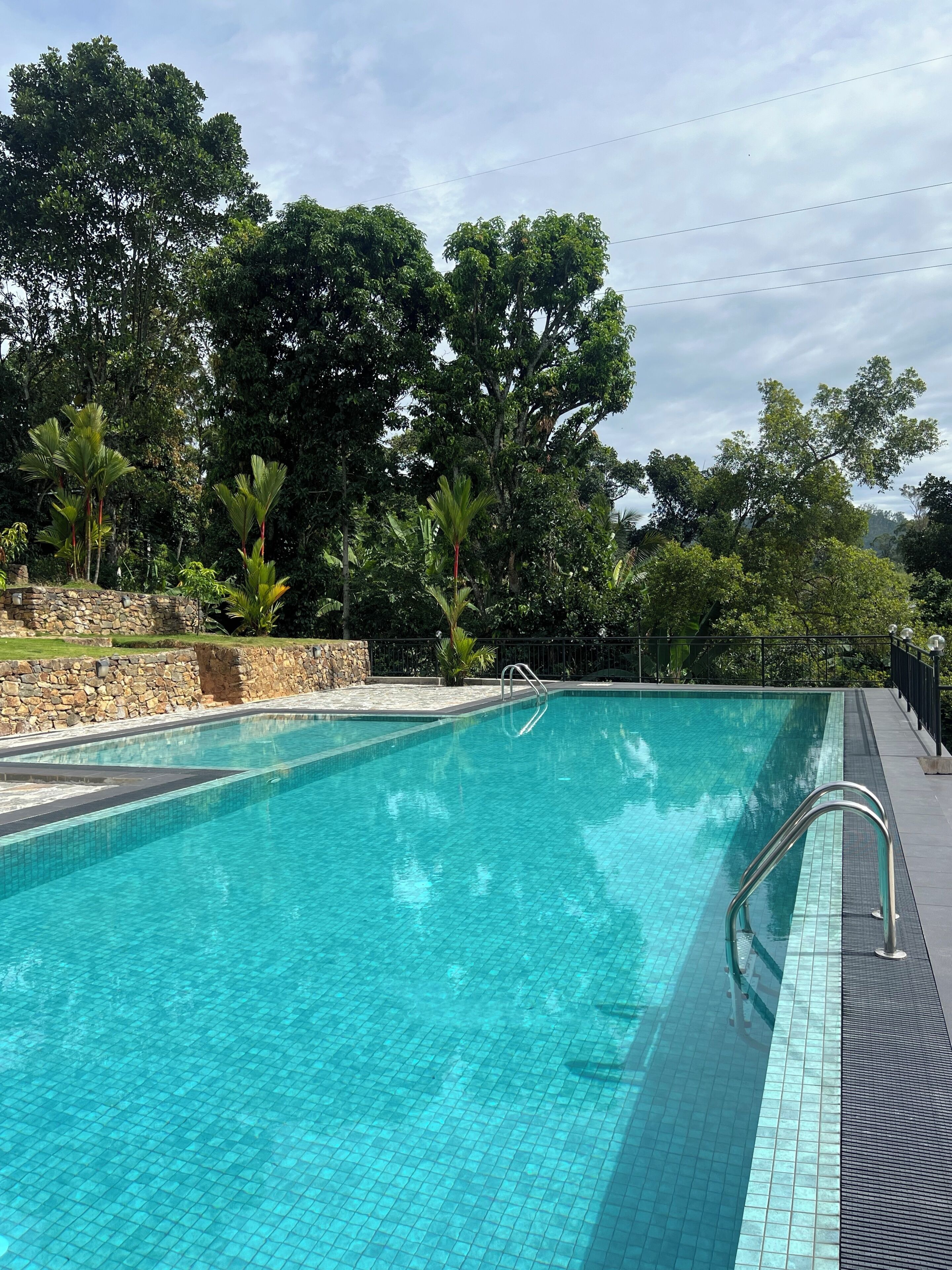 A swimming pool with clear blue water, surrounded by trees and a stone wall.