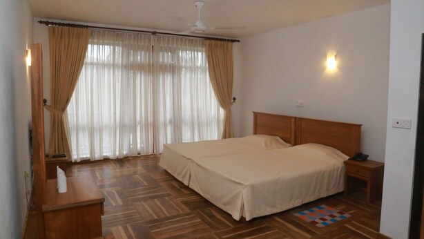 A bedroom with a wooden bed, a nightstand, a desk with a lamp, and a window with curtains. - Hotel Alta Vista (Ella)