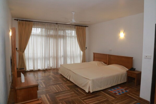 Un dormitorio con una cama de madera, una mesita de noche, un escritorio con lámpara y una ventana con cortinas.