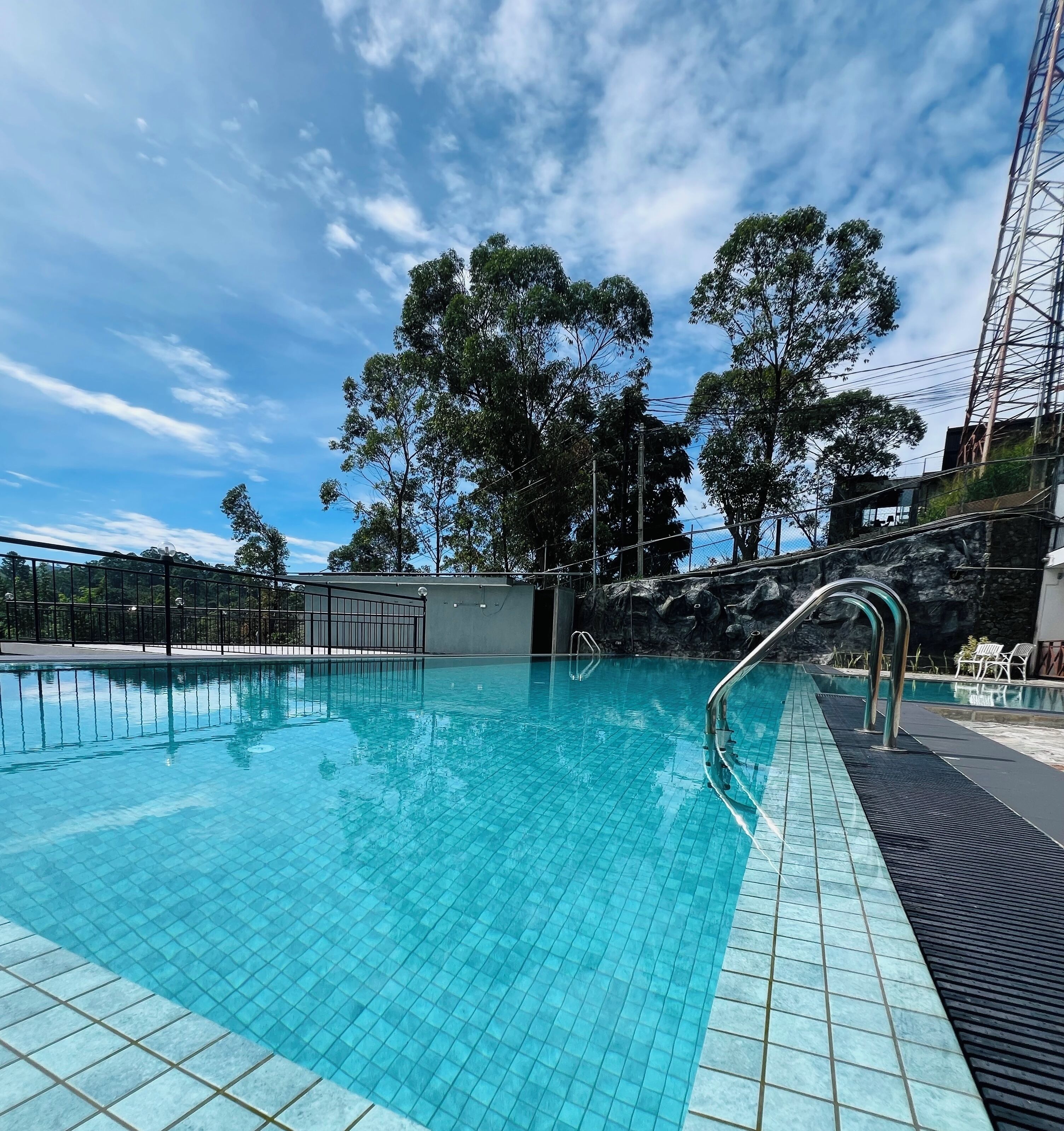 A swimming pool with tiled edges, a metal ladder, and a rock formation in the background.