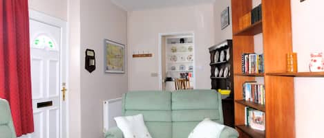 Una sala de estar con un sofá verde, una estantería de madera y una cortina roja.