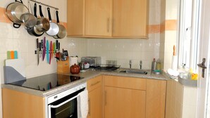 Eine kleine Küche mit Holzschränken, einem Herd, einem Spülbecken und verschiedenen Küchenutensilien, die an der Wand hängen.