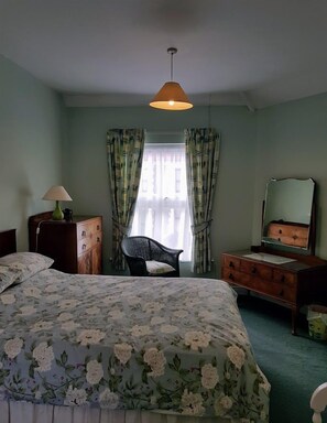 Un dormitorio con colcha estampada, una silla, un aparador, un espejo y una lámpara colgante.