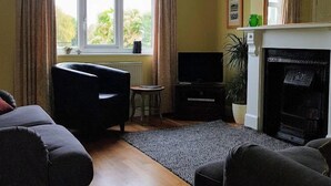 A living room with a fireplace, a television, and two sofas. - This delightful semi-detached cottage is close to walks,  bird watching & minutes from the beach. (Sheringham)