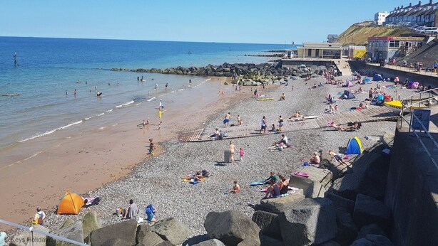 A beach with people sunbathing and swimming, a rocky shoreline, and buildings in the background. - This delightful semi-detached cottage is close to walks,  bird watching & minutes from the beach. (Sheringham)