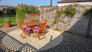 An outdoor patio with a wooden table and chairs, surrounded by a gravel area and a wooden fence. - This delightful semi-detached cottage is close to walks,  bird watching & minutes from the beach. (Sheringham)