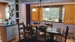 A dining area with a table set for four, surrounded by wooden chairs. A window with yellow curtains allows natural light to enter. - Family Abode for Vacation in Arachova (Distomo-Arachova-Antikyra)