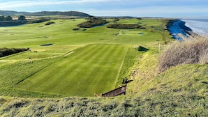 A golf course with a wooden fence, a clear view of the ocean, and a distant hill. - Romany Rye is one of the oldest and prettiest Fisherman's cottage in Sheringham in a great location (Sheringham)
