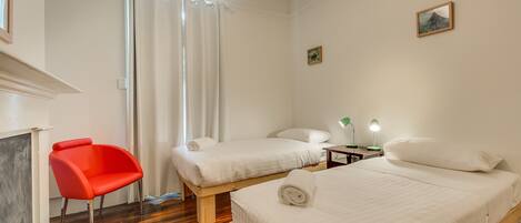 Une chambre d’hôtel avec deux lits, une chaise rouge, une table de chevet avec une lampe et un tableau au mur.