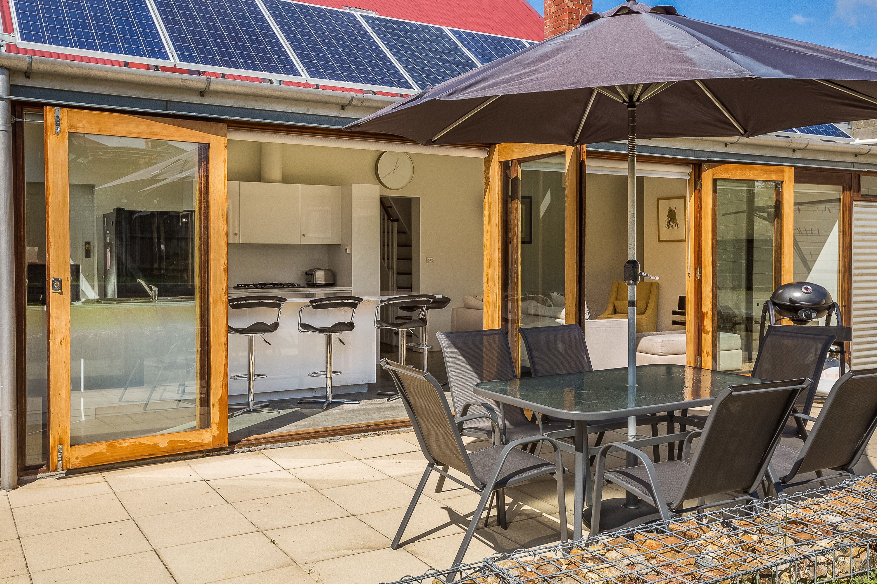 Un espace patio avec une table et des chaises en verre, un grand parasol et des panneaux solaires sur le toit.