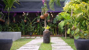 Um caminho no jardim com plantas em vasos e jardineiras suspensas.
