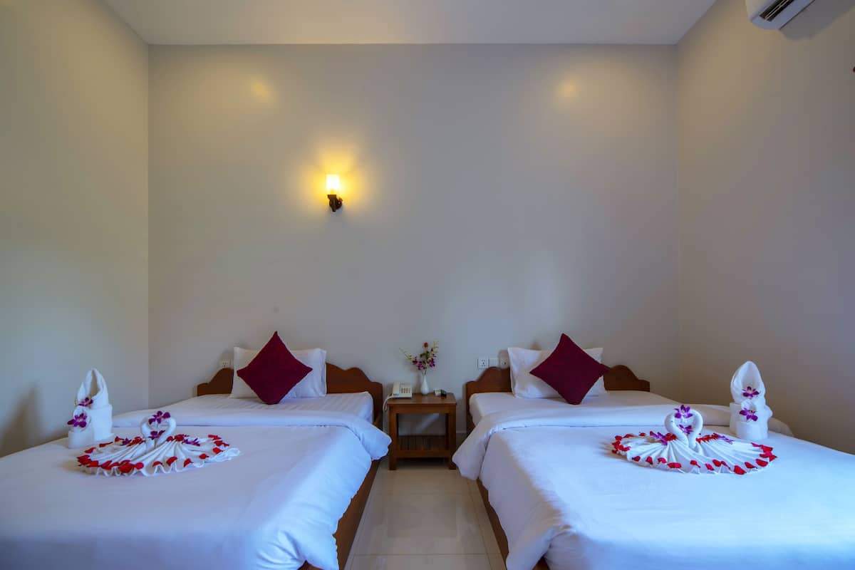 Habitación de hotel con dos camas, ropa blanca, almohadas rojas y adornos de cisnes decorativos.