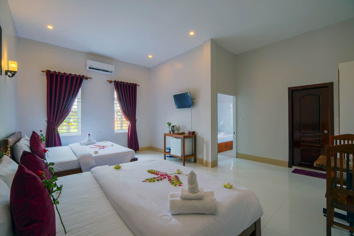 Habitación de hotel con dos camas, un televisor, una mesita de madera y un baño visible a través de una puerta de vidrio.