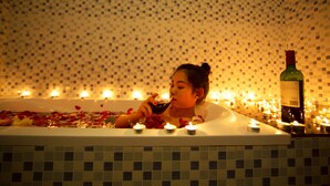 Uma banheira com velas e uma garrafa de vinho, rodeada por pétalas de rosa.
