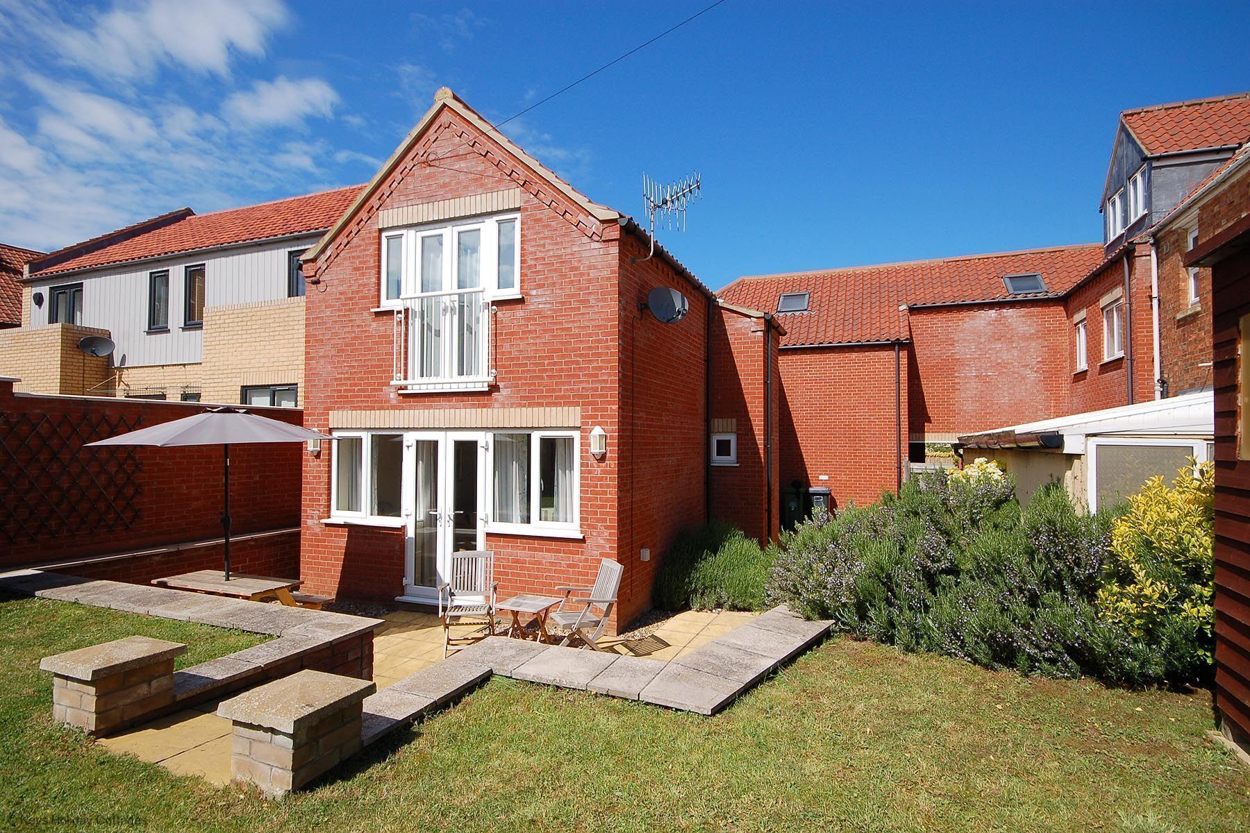 A two-story brick house with a red-tiled roof, a front door, and a small front yard with a patio and steps leading to the door.