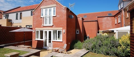 A two-story brick house with a red-tiled roof, a front door, and a small front yard with a patio and steps leading to the door.