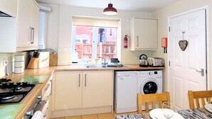Cocina compacta con estufa a gas, lavadora y comedor con mesa y sillas.