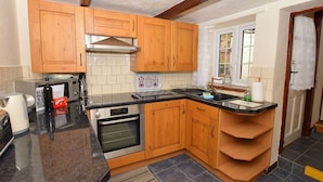 Una cocina compacta con armarios de madera, horno integrado, campana extractora de acero inoxidable y encimera negra.