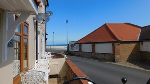 Una calle costera con un edificio que cuenta con una terraza, asientos al aire libre y vistas al mar.