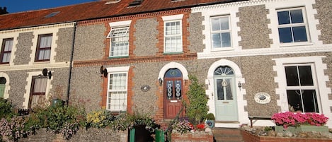 A row of terraced houses with distinct stone and brick facades, multiple windows, and a small garden area with flowers.