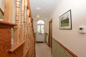 Una escalera de madera que conduce a una puerta con un ventanal, un cuadro en la pared y un termostato.