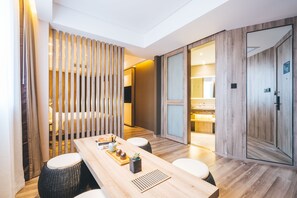 A modern hotel room with a wooden dining table, two wicker stools, a small side table with decorative items, a sliding door leading to a bathroom, and a large mirror. - Atour Hotel Hongqiao Hub National Exhibition Center Shanghai (Shanghai)