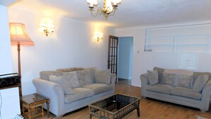 A living room with two sofas, a coffee table, a lamp, and a radio. - Set within an area of Outstanding Natural Beauty this bungalow is just the place in which to relax (Cromer)