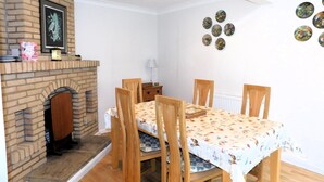 A dining area with a brick fireplace, wooden chairs, and a table covered with a floral tablecloth. - Set within an area of Outstanding Natural Beauty this bungalow is just the place in which to relax (Cromer)