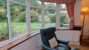 A room with a large bay window, a black leather chair, a wooden table, and a lamp. - Set within an area of Outstanding Natural Beauty this bungalow is just the place in which to relax (Cromer)