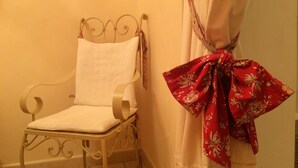 A metal-framed chair with a white cushion, positioned next to a wall with a white curtain and a red floral cloth tied to it. - Le Vieux Pressoir Vacation Rental: Nestled among vineyards, scrubland, and a relaxed lifestyle, with a view of Uzès (Montaren-et-Saint-Médiers)
