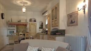 A cozy living room with a sofa, a dining table, and chairs. There is a kitchen area with cabinets and a radiator. - Le Vieux Pressoir Vacation Rental: Nestled among vineyards, scrubland, and a relaxed lifestyle, with a view of Uzès (Montaren-et-Saint-Médiers)
