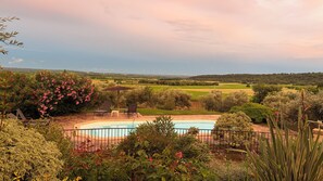 A swimming pool surrounded by lush greenery and a view of distant fields.