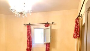 A bedroom with two beds, a radiator, a chair, and a window with curtains. - Le Vieux Pressoir Vacation Rental: Nestled among vineyards, scrubland, and a relaxed lifestyle, with a view of Uzès (Montaren-et-Saint-Médiers)