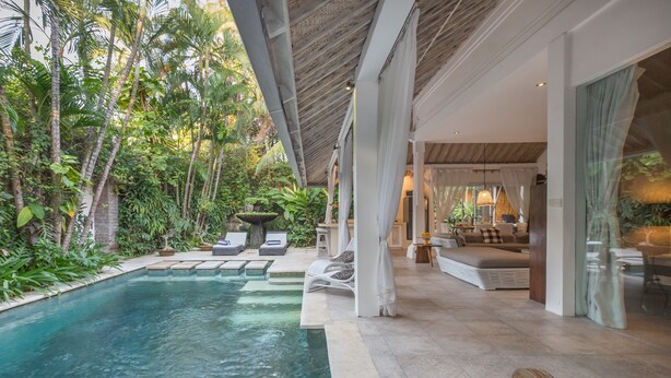 A poolside area with lounge chairs, a seating area with cushions, and a view of lush greenery. - Villa Esha Drupadi I (Seminyak)