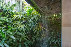 A showerhead with water flowing into a lush green garden area.