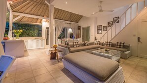 A spacious living area with a large sofa set, a dining table, and a kitchen area visible through an open archway. - Villa Esha Drupadi I (Seminyak)