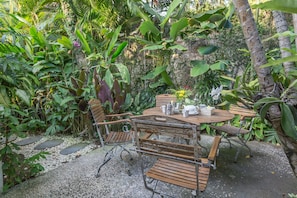 A wooden table with metal chairs, surrounded by lush greenery and a stone pathway.