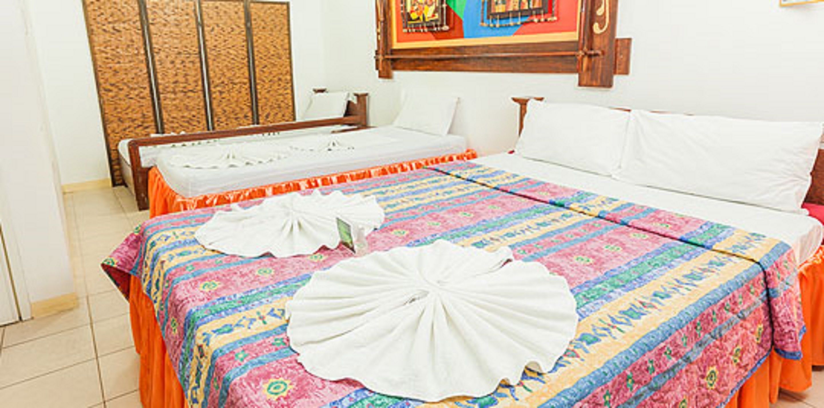 A hotel room with a large bed, a colorful bedspread, and a decorative towel on the bed.