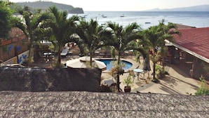 A pool area with palm trees, a swimming pool, and a view of the sea with boats. - Oriental Sabang Hill Resort (Puerto Galera)